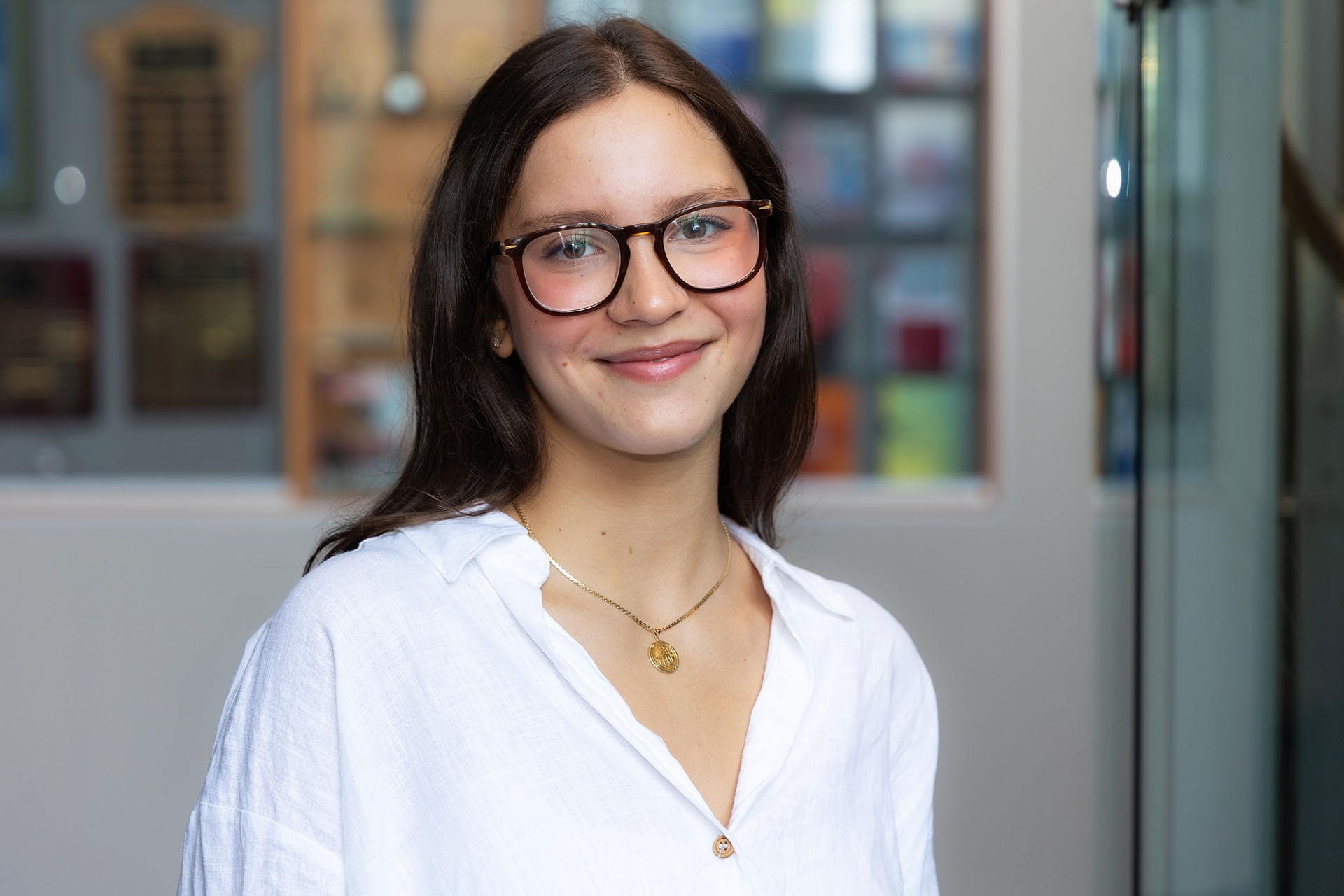 Leila has long dark hair and glasses. She is wearing a white blouse and smiling.