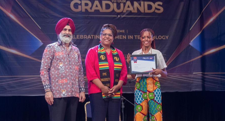 A woman holding a certificate stands on stage next to two other people