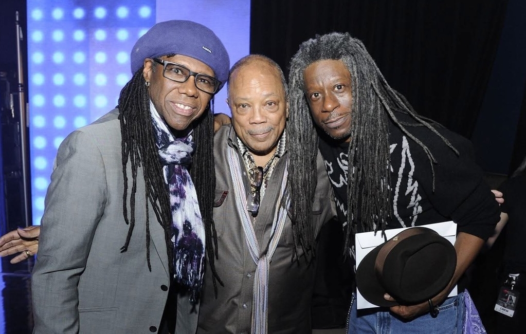 Three men pose in front of a black background with purple and blue lights