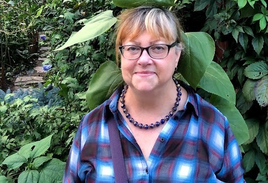 Professor Sara Terreault standing in front of trees and a large sunflower 