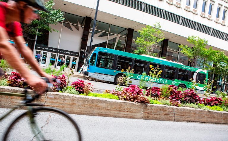 Une personne à vélo entre dans le cadre par la gauche et, à l'arrière-plan, un bus de ville.