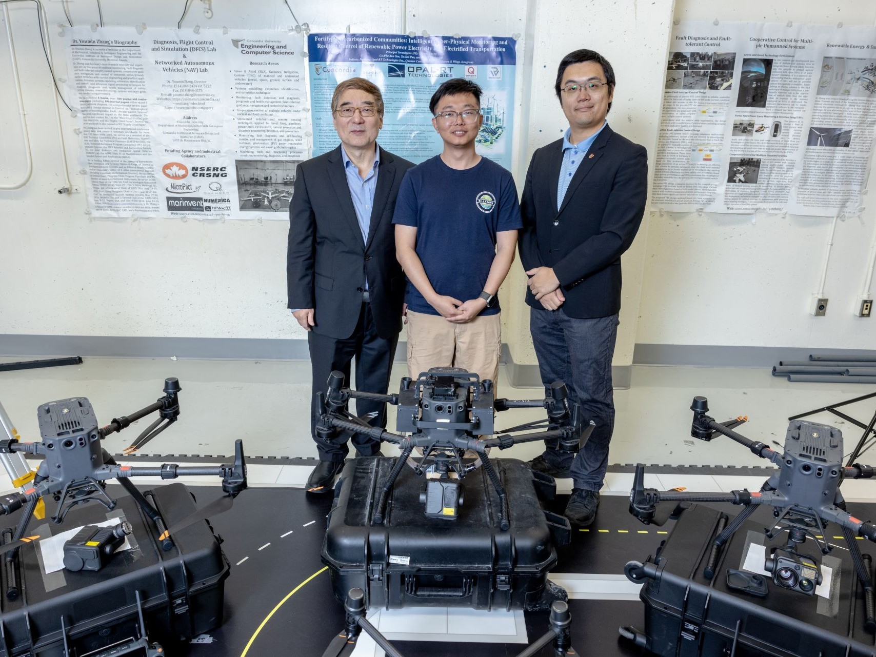 Three researchers stand in a room of UAVs