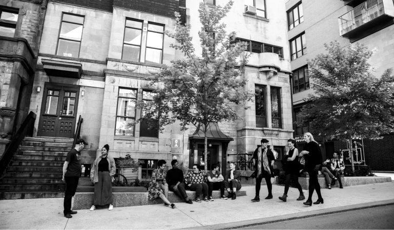 A photo in black and white of people sitting, walking and gathering on a quiet city street