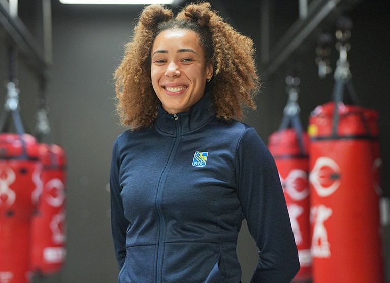 Female athlete smiling, standing in front of four red punching bags