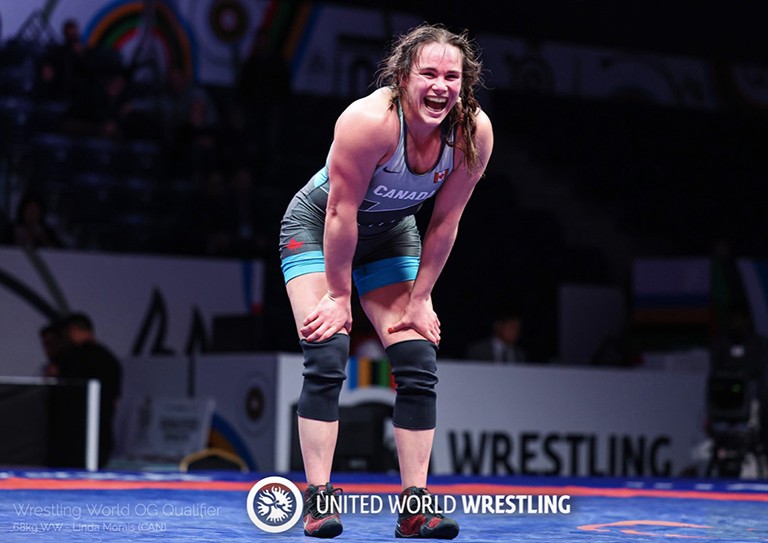 Young woman in wresting gear with a big smile, leaning forward with hands on knees