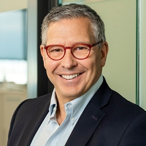 Smiling man with short, blond hair, wearing red-rimmed glasses