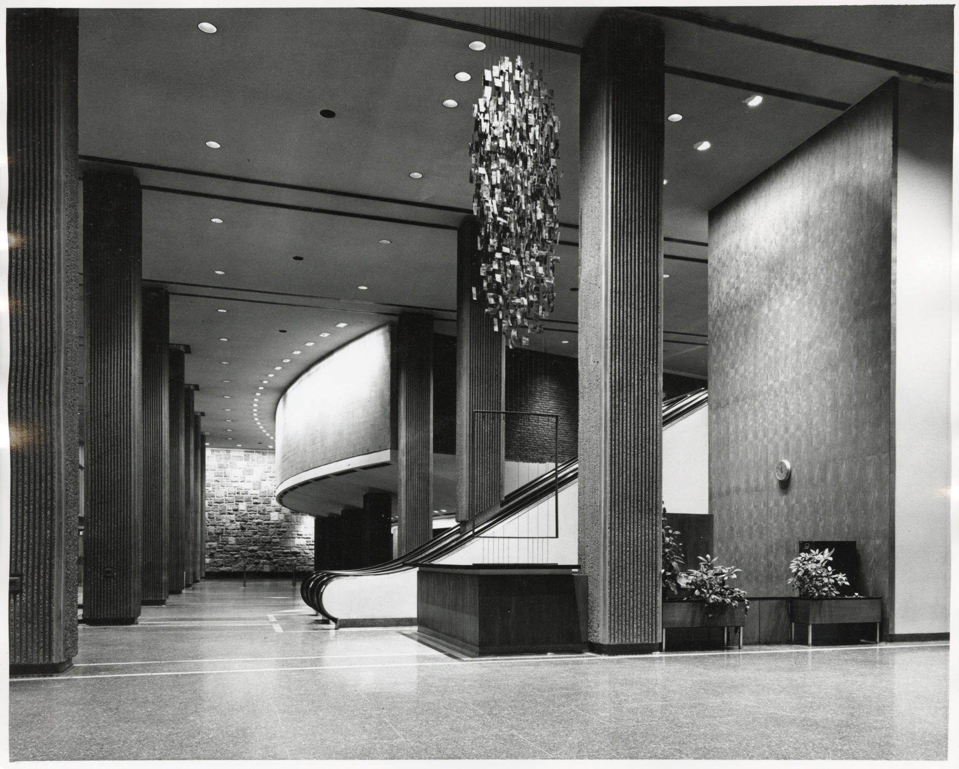 Photo vintage en noir et blanc d'un élégant hall d'entrée avec un escalier incurvé et des luminaires décoratifs, reflétant le design moderne du milieu du siècle.