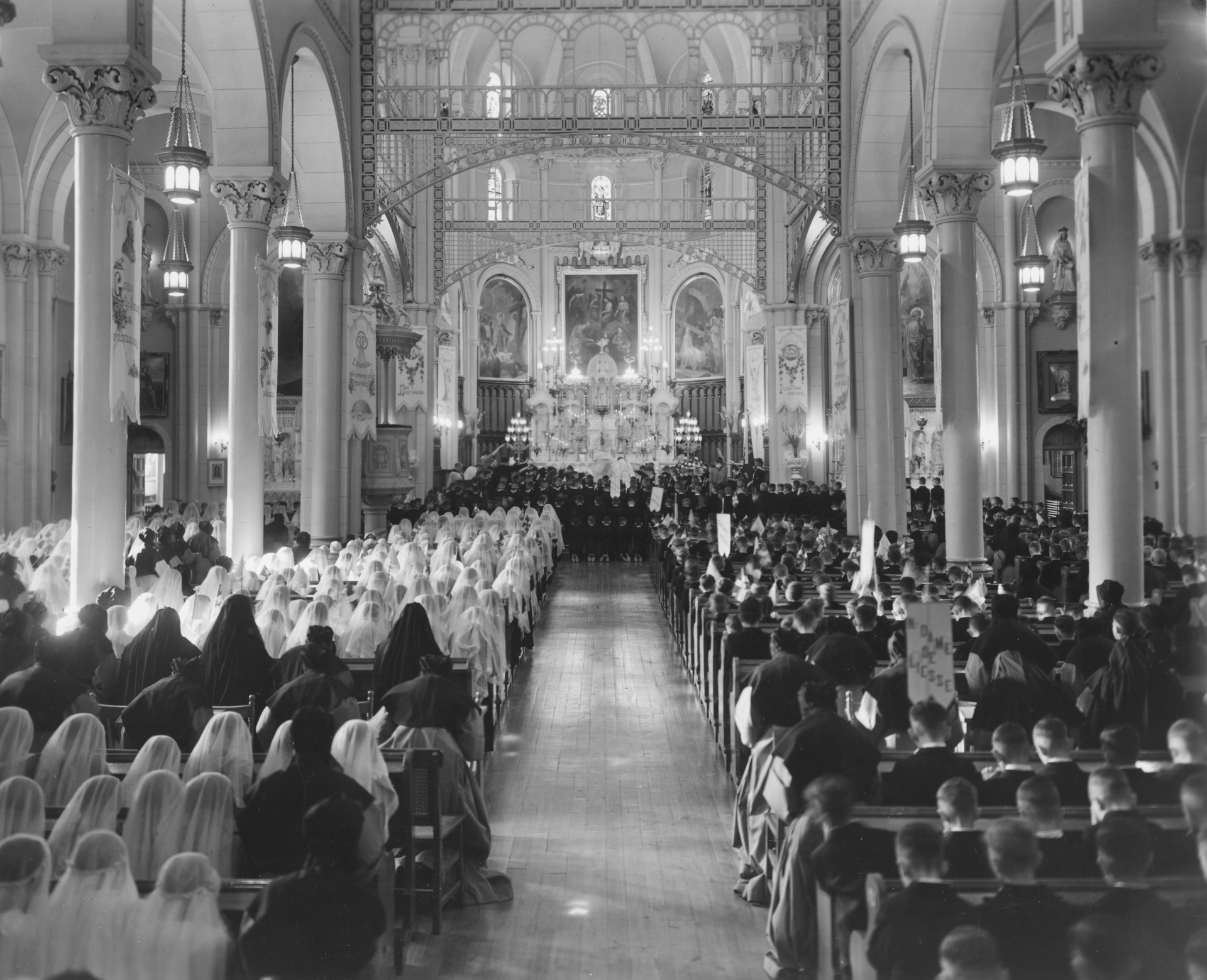 Photographie historique montrant une assemblée nombreuse assistant à une cérémonie dans une église à l'intérieur orné de vitraux.