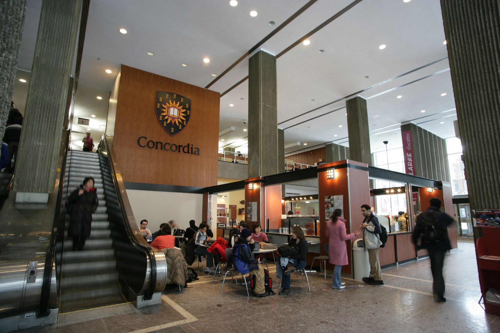 L'intérieur animé du Pavillon Hall de l'Université Concordia, avec des étudiants et un café sous le logo de l'université.