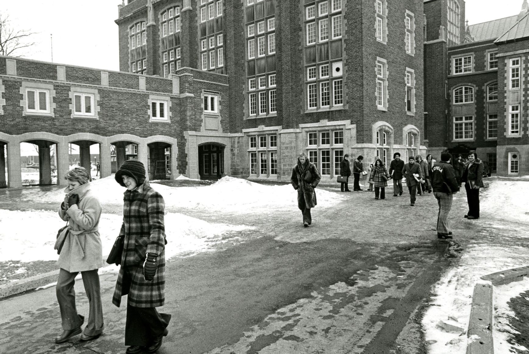 Étudiants marchant en tenue d'hiver sur un campus enneigé, avec une architecture traditionnelle en arrière-plan.