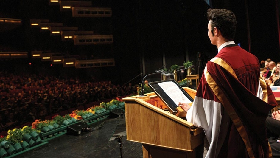 Un jeune homme vêtu d'une robe de fin d'études se tient sur un podium pour prononcer le discours du major de sa promotion.