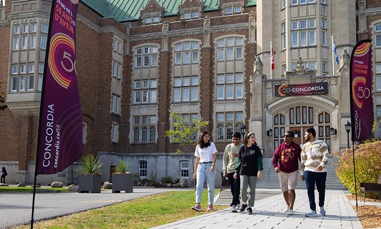 Cinq étudiants de Concordia portant des t-shirts à l'effigie du 50e anniversaire se dirigent vers nous devant le bâtiment administratif du campus de Loyola.