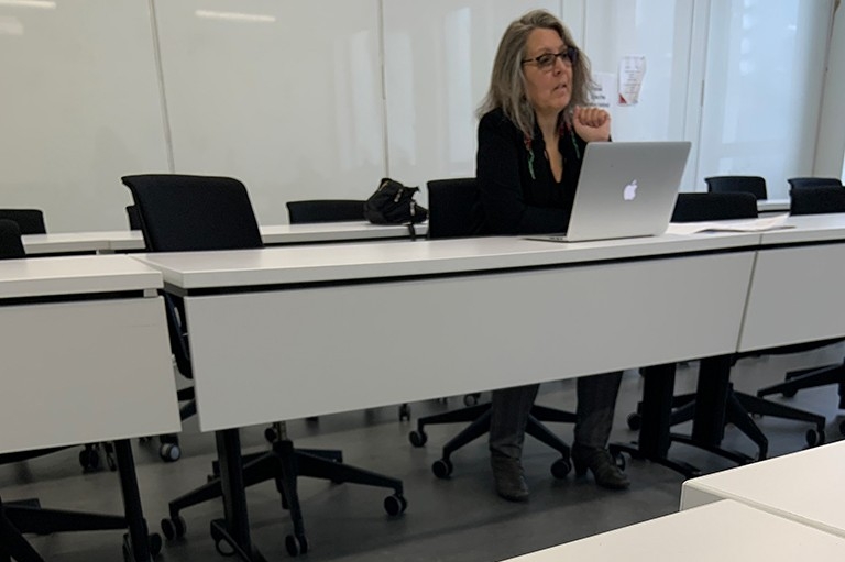 Une femme à un bureau dans une salle de classe avec de longs pupitres.