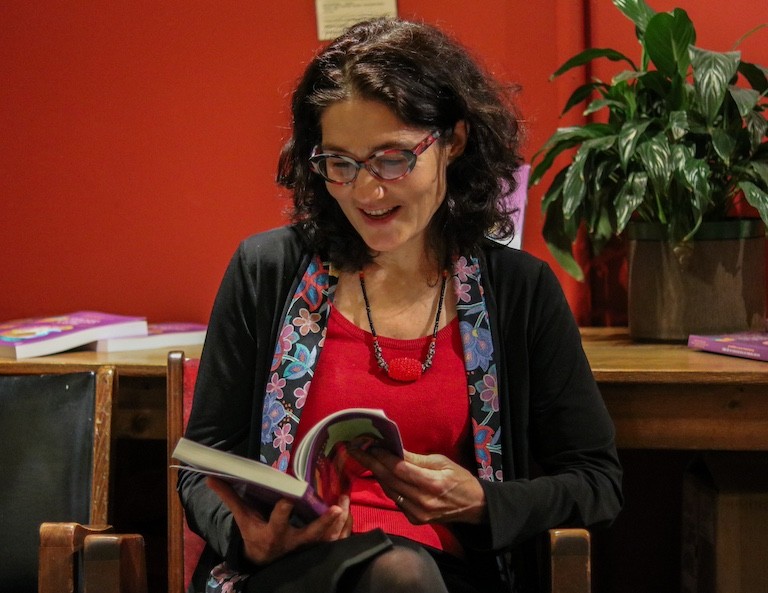 Une femme aux cheveux noirs et aux lunettes, assise sur une chaise, lisant un livre