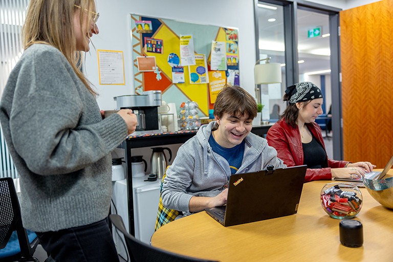 Smiling young people in a small space on laptops